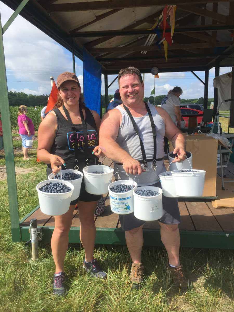 Satisfied guests taking full advantage of the discount for picking large quantities. Buckets upon buckets of blueberries are fastened to their waist. 